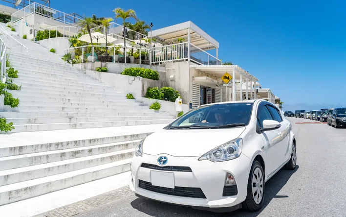 A white first generation Toyota Aqua hybrid parked by a flight of steps