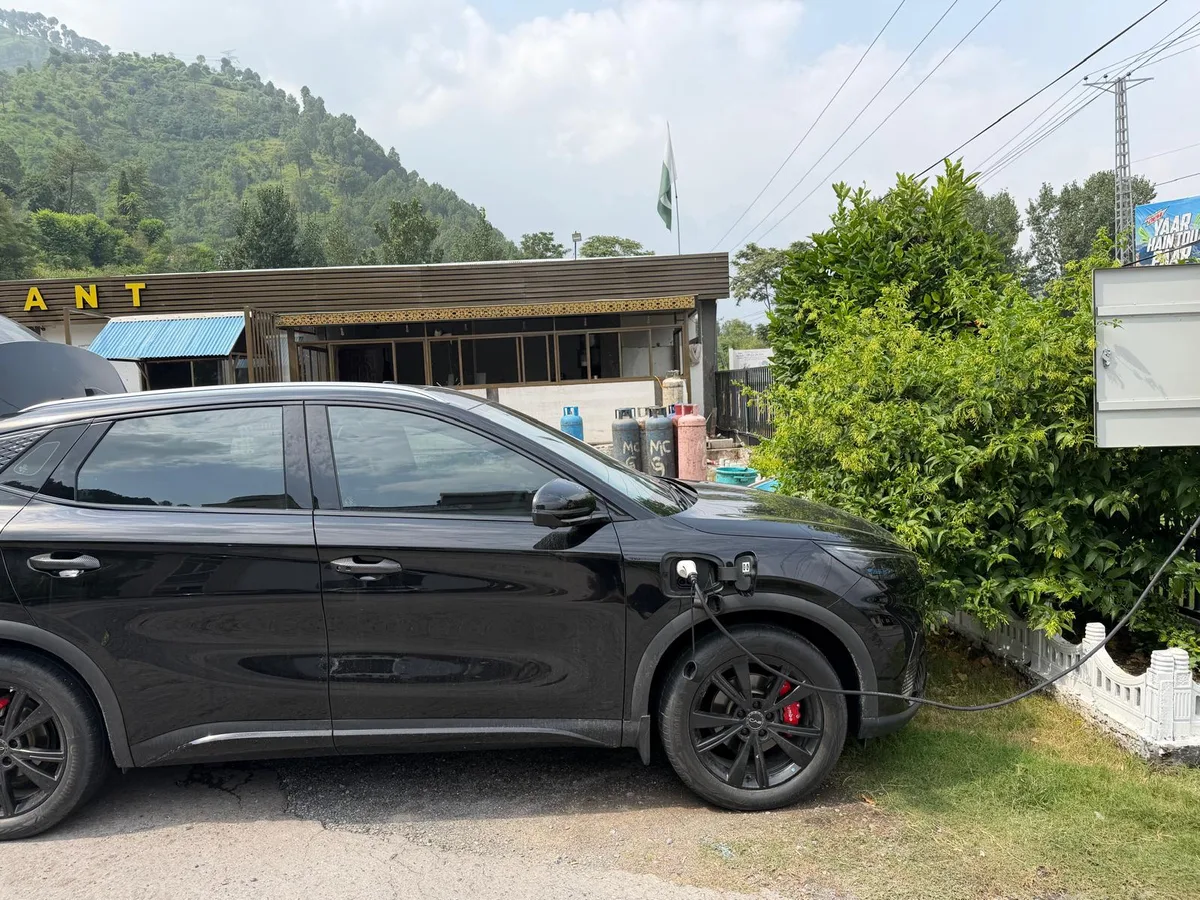 A BYD charging from a wall connector beside greenery in Balakot