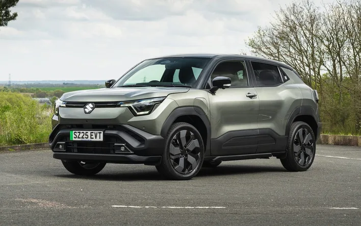 Suzuki e Vitara electric SUV in two tone green, front three quarter view, parked beside a country road